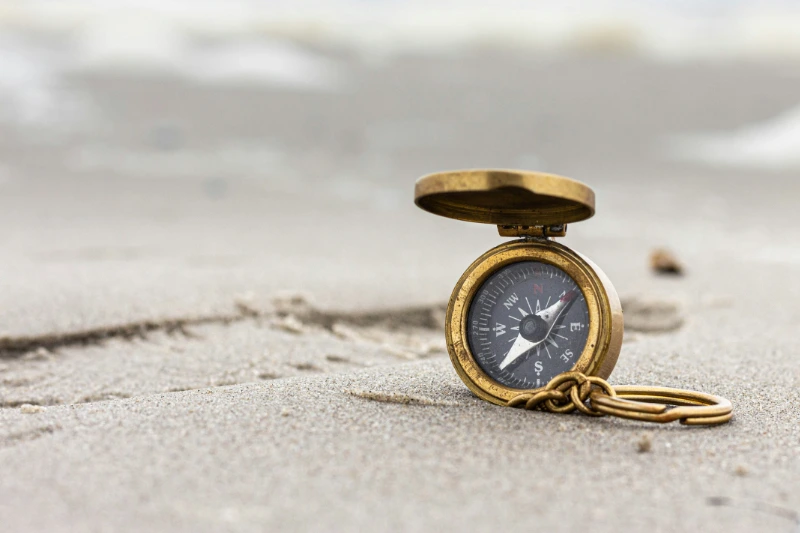Danske veteraner rammes af moralsk skade Gammeldags kompas i messing ligger i sandet på en strand med sløret hav i baggrunden.