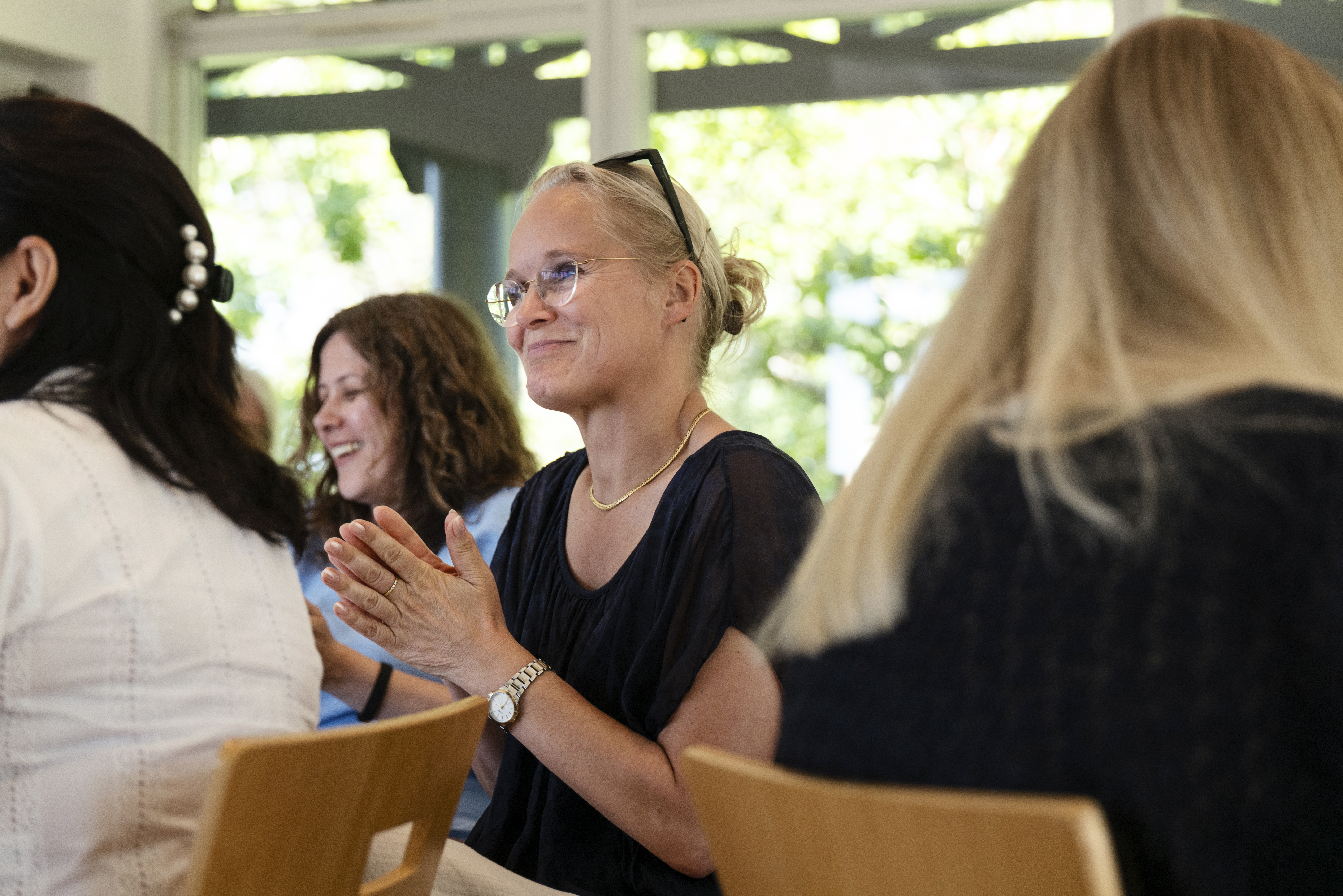 Tre kvinder smiler og holder certifikat ved vindue i undervisningslokale