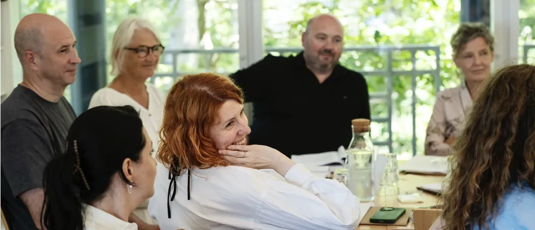 Gruppe af voksne samlet omkring et bord i et lyst mødelokale, mens de deltager i en samtale.